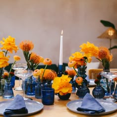 a wooden table topped with blue vases filled with yellow flowers next to a white candle