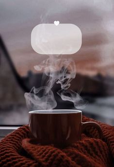 a cup of coffee with steam rising out of it on a blanket next to a window