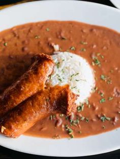 two sausages in gravy on a plate with rice and garnish