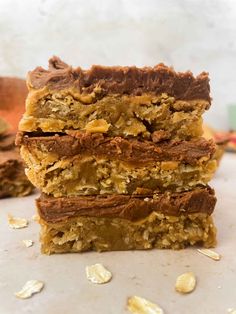 three pieces of chocolate peanut butter bars stacked on top of each other with oats scattered around them