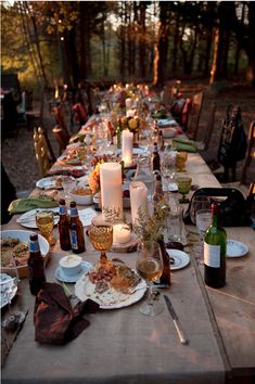 a long table is set with plates and candles for an outdoor dinner party in the woods