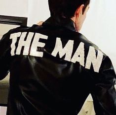 a man wearing a jacket that says the man in white letters on it's back