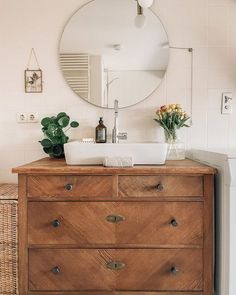 a bathroom with a wooden dresser, mirror and flowers on the counter top in front of it