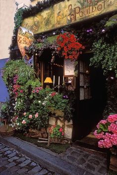 the outside of a flower shop with lots of flowers growing on it's side