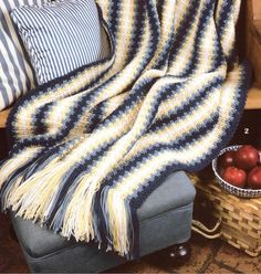 a blue and yellow blanket sitting on top of a chair next to apples in a basket