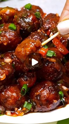 a person is holding chopsticks in a bowl of meatballs with sauce and green onions