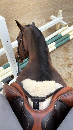 a brown horse standing next to a white fence and wearing a saddle on it's back