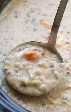 a ladle full of soup in a crock pot with carrots on the side