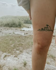 a person with a small tattoo on their leg standing in the grass and looking off into the distance