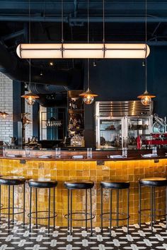 a bar with several stools and lights hanging from it's ceiling in a restaurant