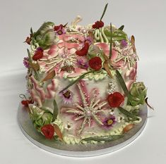 a cake decorated with flowers and leaves on a silver platter, sitting on a white surface