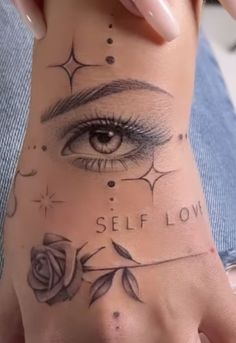 a woman's hand with an eye and rose tattoo on her left wrist that says self love