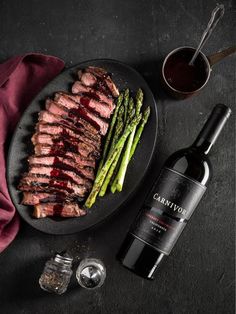 steak and asparagus on a plate next to a bottle of wine with a spoon