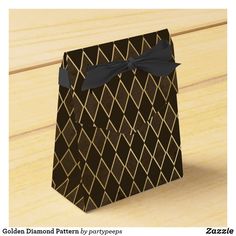 a black and gold diamond pattern paper bag with a bow on the front, sitting on a wooden surface