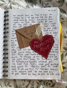 an open notebook with some paper on top of it and a red heart in the middle