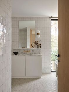 a bathroom with white tile walls and flooring next to a large mirror on the wall