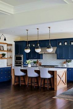 a kitchen with dark blue cabinets and white counter tops, wooden flooring and bar stools