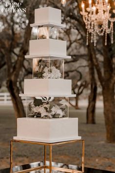 a three tiered white wedding cake with flowers and greenery on the top, surrounded by chandeliers