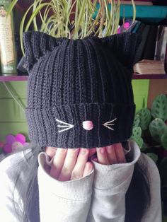 a woman covering her face while wearing a knitted hat with cat ears on it