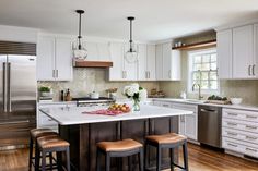 a kitchen with white cabinets and stainless steel refrigerator freezer next to two bar stools