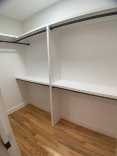 an empty walk in closet with white shelving and wood flooring on the side