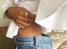 a woman in white shirt and blue jeans holding her stomach with gold ring on it