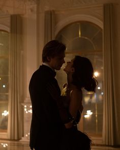 a man and woman standing next to each other in front of a window at night