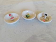 three small white bowls with tiny figurines in them