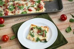 a slice of pizza sitting on top of a white plate next to a pan filled with tomatoes and spinach