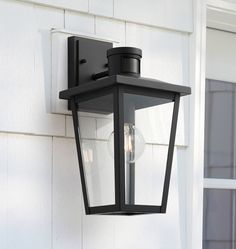 a black outdoor light mounted on the side of a white building with two lights attached to it