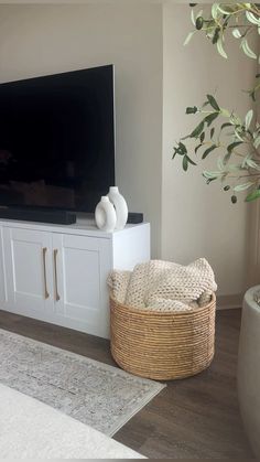 a flat screen tv sitting on top of a white entertainment center next to a potted plant