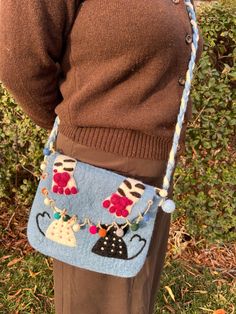 a woman wearing a brown sweater is holding a blue purse with small objects on it