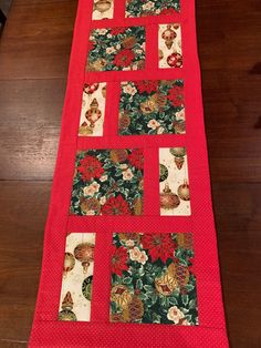 a red table runner with flowers and leaves on the top, sitting on a wooden floor