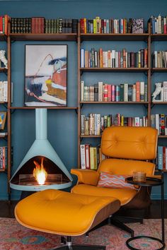 an orange chair and ottoman in front of a fireplace with bookshelves behind it