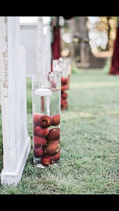 apples are in a glass vase on the grass near an arch with candles and drapes