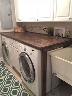 a washer and dryer in a small room with white cupboards, drawers, and a wooden counter top