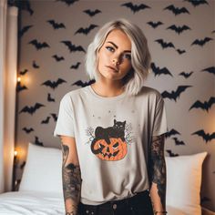 a woman with white hair wearing a halloween t - shirt and black jeans, standing in front of a bed