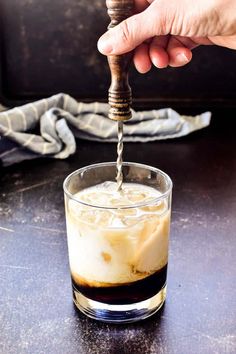 someone is pouring something into a glass with ice and liquid in it on the table