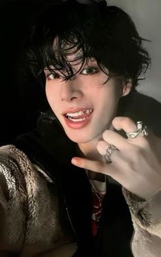 a man with black hair and piercings on his fingers pointing to the side while wearing a jacket