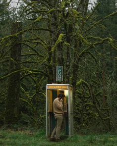 a man standing in the doorway of a phone booth next to a forest filled with trees