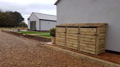 a wooden storage box sitting on the side of a building next to a gravel road