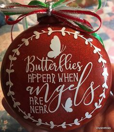 a hand holding a red ornament with white lettering on it that says butterflies appear when angels are near