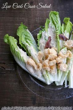 lettuce with crumbs and bacon on it in a glass bowl sitting on a wooden table