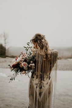 a woman with long hair wearing a fringed dress and holding flowers in her hand