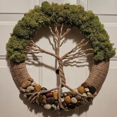 a wreath made out of branches and rocks is hanging on a door with a tree in the middle