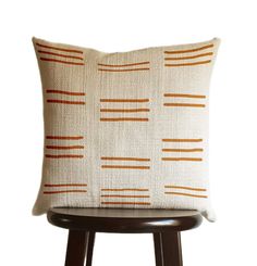 a white pillow sitting on top of a wooden stool next to a black and brown chair