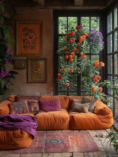 an orange couch sitting in front of a window filled with lots of plants and flowers