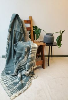 a chair and table with a blanket on it next to a potted green plant