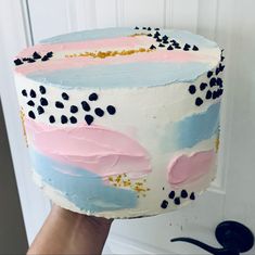 a person holding up a cake with pink, blue and white frosting