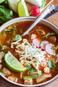 a close up of a bowl of soup on a table with vegetables and limes